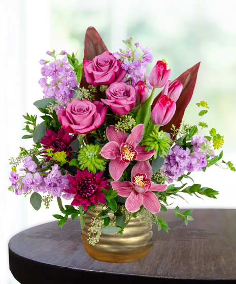A stunning everyday flower arrangement featuring magenta roses, pink tulips, lavender stock, and a cymbidium orchid in a gold pedestal vase.