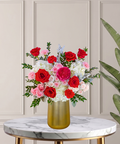 Another Year Loving You flower arrangement with red roses, pink garden roses, blush spray roses, and hydrangeas in a tall white vase