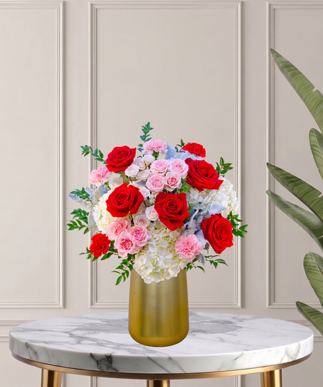 Another Year Loving You flower arrangement with red roses, pink garden roses, blush spray roses, and hydrangeas in a tall white vase