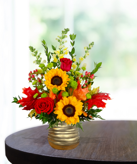 Fall flower arrangement with sunflowers, red roses, snapdragons, berries, and autumn leaves in a gold hammered vase.