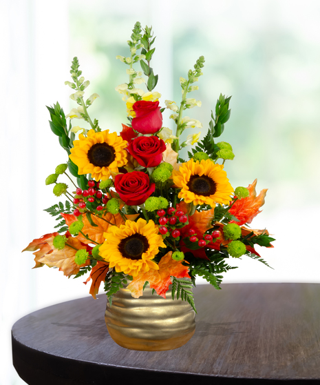 Fall flower arrangement with sunflowers, red roses, snapdragons, berries, and autumn leaves in a gold hammered vase.
