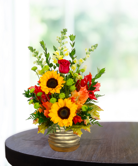 Fall flower arrangement with sunflowers, red roses, snapdragons, berries, and autumn leaves in a gold hammered vase.