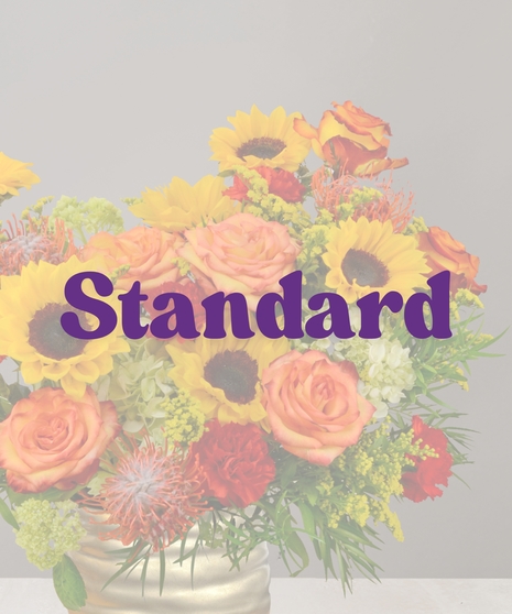 Autumn floral arrangement with sunflowers, orange roses, red carnations, and greenery in a gold vase