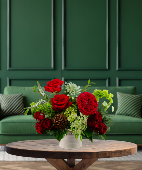 Mulberry Pine rustic Christmas flower arrangement with red roses, green hydrangeas, Bells of Ireland, red berries, and pine cones in a textured vase