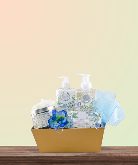 Serenity for Mom gift basket with cotton & linen-scented spa products, floral accents, and ivory ribbon in a woven basket – Mother’s Day gift idea.
