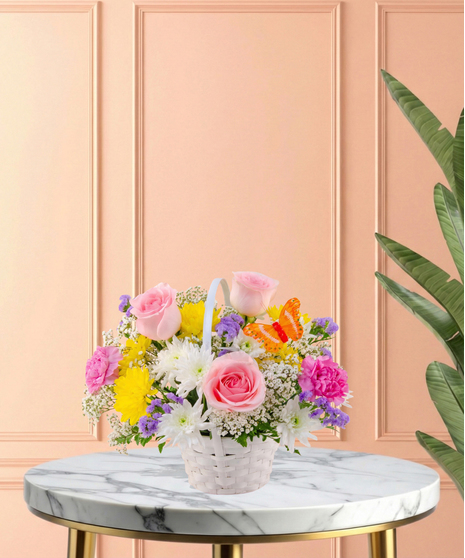 Basket of Blooms Easter flower arrangement featuring roses, mums, carnations, baby's breath, and an orange butterfly decoration in a classic white woven basket