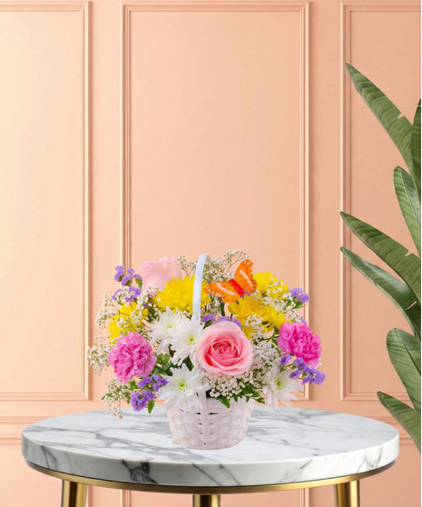 Basket of Blooms Easter flower arrangement featuring roses, mums, carnations, baby's breath, and an orange butterfly decoration in a classic white woven basket