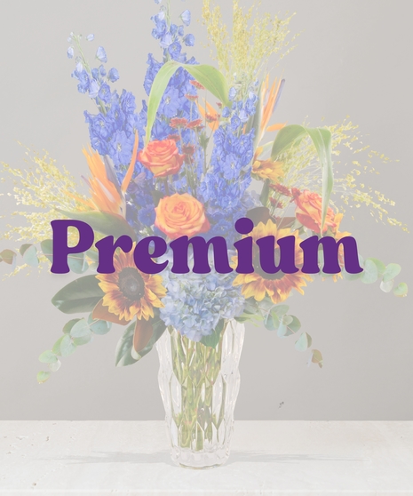 Bess fall flower arrangement with blue delphinium, sunflowers, Birds of Paradise, hydrangea, and orange roses in a crystal vase