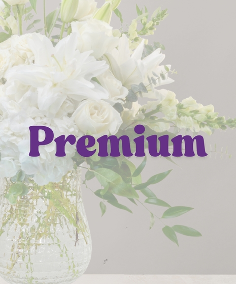 Elegant white flower arrangement with lilies, roses, hydrangeas, and eucalyptus in a tall clear vase
