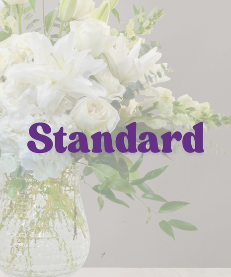 Elegant white flower arrangement with lilies, roses, hydrangeas, and eucalyptus in a tall clear vase