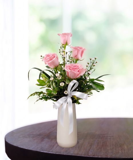 Bud Vase with six pink roses, white baby's breath, and a pink satin ribbon in a tall white ceramic vase.