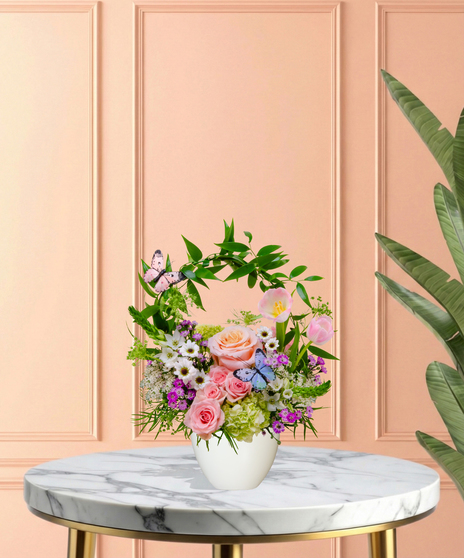 Butterfly Brunch flower arrangement with peach roses, tulips, hydrangeas, daisies, and butterfly accents in a pedestal vase with arched greenery.