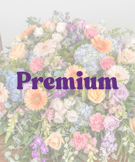 Colorful pastel casket spray with roses, gerbera daisies, hydrangea, and carnations on a wooden casket from Billy Heroman’s Florist in Baton Rouge