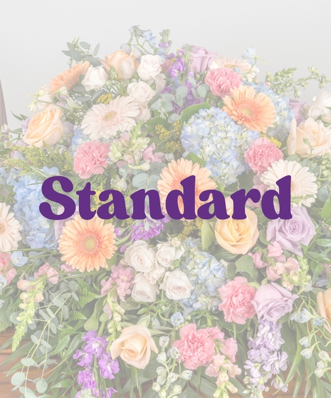 Colorful pastel casket spray with roses, gerbera daisies, hydrangea, and carnations on a wooden casket from Billy Heroman’s Florist in Baton Rouge