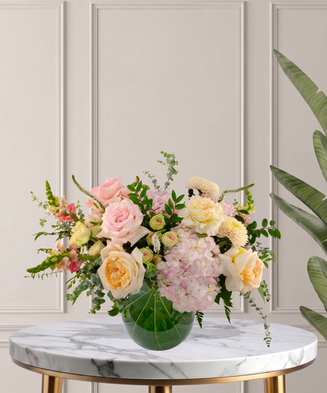 Charlotte Signature flower arrangement featuring peach garden roses, pink hydrangeas, blush roses, and white veronica in a glass bubble bowl.