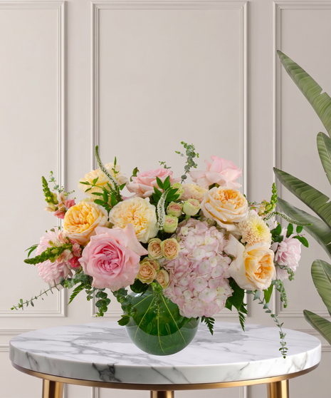 Charlotte Signature flower arrangement featuring peach garden roses, pink hydrangeas, blush roses, and white veronica in a glass bubble bowl.