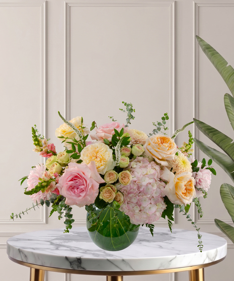 Charlotte Signature flower arrangement featuring peach garden roses, pink hydrangeas, blush roses, and white veronica in a glass bubble bowl.