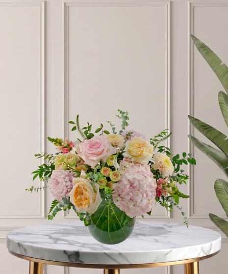 Charlotte Signature flower arrangement featuring peach garden roses, pink hydrangeas, blush roses, and white veronica in a glass bubble bowl.