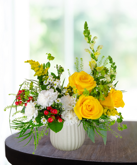 Banana Split flower arrangement with yellow roses, white carnations, red berries, and assorted greenery in a white vase