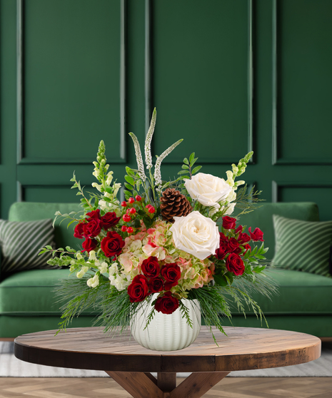 Christmas Crush flower arrangement with white roses, red roses, blush hydrangeas, white snapdragons, pine cones, red berries, and evergreen in a textured white vase