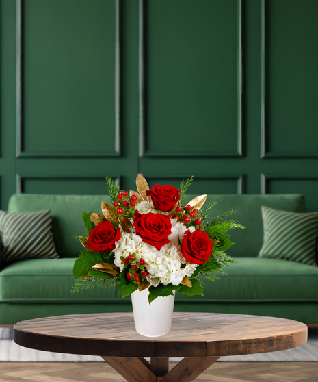Claus's Choice red and white Christmas flower arrangement with red roses, white hydrangeas, red berries, gilded leaves, and evergreen in a white container