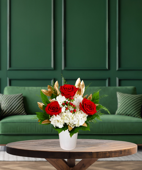 Claus's Choice red and white Christmas flower arrangement with red roses, white hydrangeas, red berries, gilded leaves, and evergreen in a white container