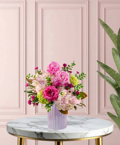 Crown Jewel Signature flower arrangement featuring large pink peonies, magenta garden roses, and lush pink hydrangeas in a ridged lavender glass vase.