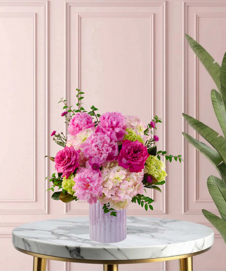Crown Jewel Signature flower arrangement featuring large pink peonies, magenta garden roses, and lush pink hydrangeas in a ridged lavender glass vase.