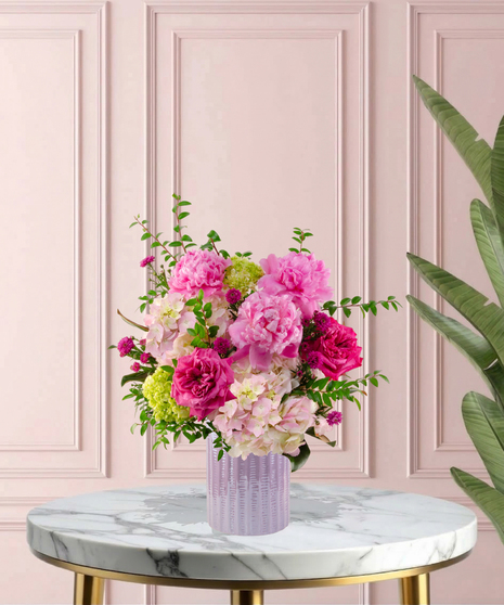 Crown Jewel Signature flower arrangement featuring large pink peonies, magenta garden roses, and lush pink hydrangeas in a ridged lavender glass vase.