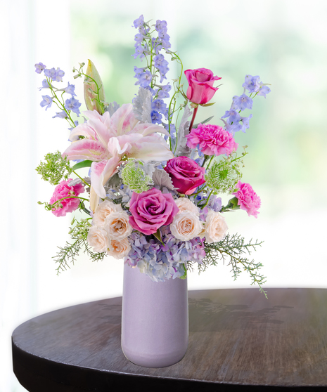 Lavender Haze flower arrangement with lilies, pink roses, blue hydrangeas, and delphinium in a lavender vase