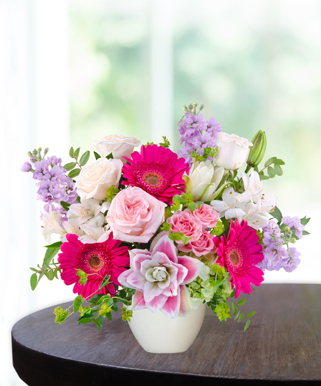 Pink Carats floral arrangement featuring pink roses, gerbera daisies, lilies, hydrangeas, and spring blooms in an ivory vase – an April birthday exclusive.