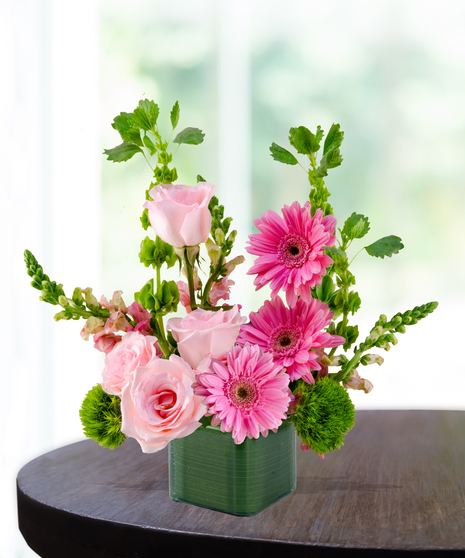 Bright pink gerbera daisies and blush roses arranged in a green ceramic cube