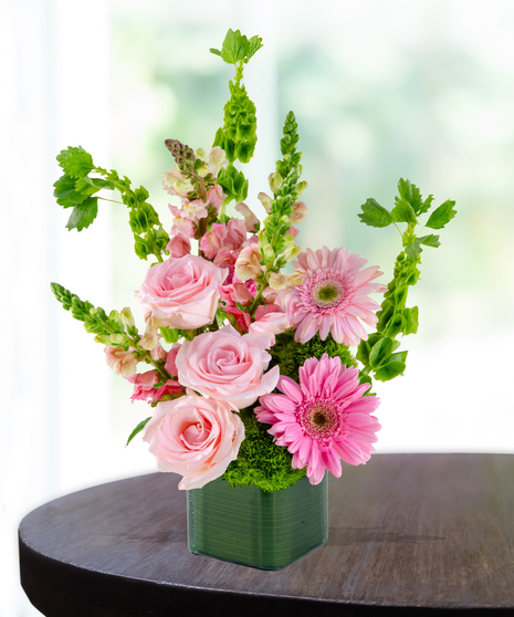 Bright pink gerbera daisies and blush roses arranged in a green ceramic cube
