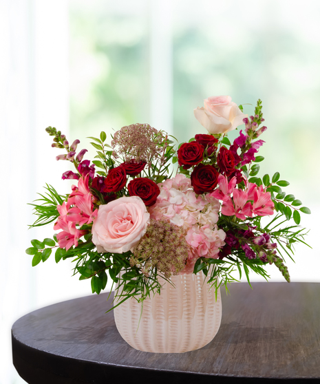 Vibrant floral arrangement featuring cranberry and blush roses in a textured cream vase for a January birthday gift.