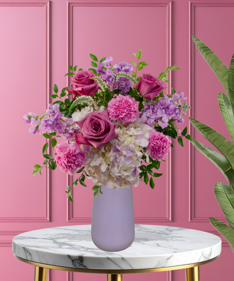 Pretty in Purple exclusive Valentine's and February birthday flower arrangement with lavender roses, white lilies, purple stock, and magenta mums in a frosted lavender vase.