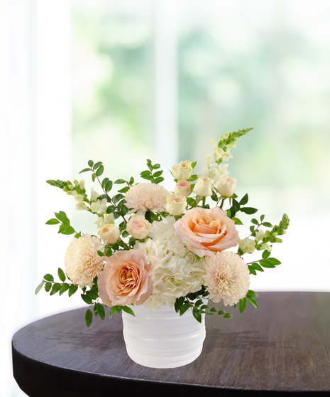 She's A Peach exclusive April birthday flower arrangement with peach garden roses, cream spray roses, white hydrangeas, and snapdragons in a ridged white vase.