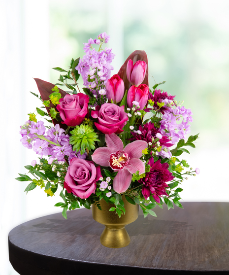 A stunning everyday flower arrangement featuring magenta roses, pink tulips, lavender stock, and a cymbidium orchid in a gold pedestal vase.
