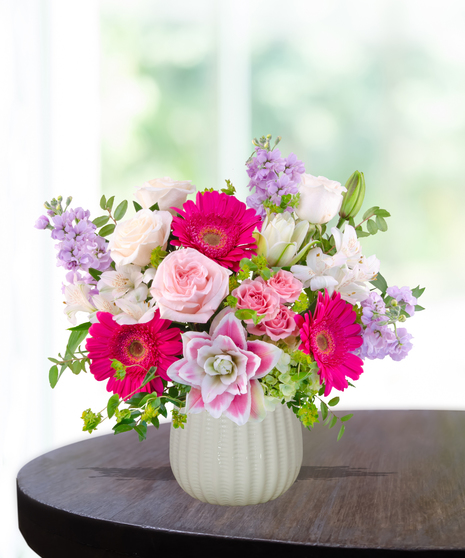 Pink Carats floral arrangement featuring pink roses, gerbera daisies, lilies, hydrangeas, and spring blooms in an ivory vase – an April birthday exclusive.