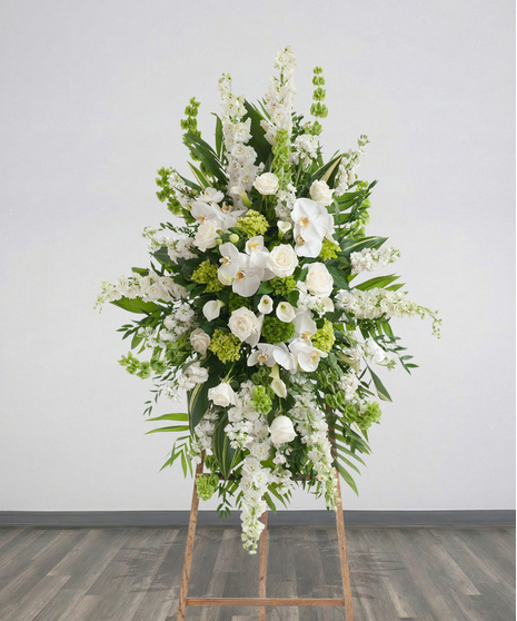 Elegant White Funeral Standing Spray with white roses, orchids, lilies, and bells of Ireland on a wooden easel