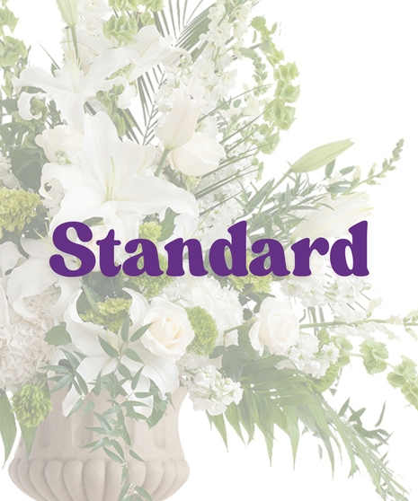 Elegant White Urn Arrangement with white lilies, roses, hydrangeas, and bells of Ireland in a tall stone urn