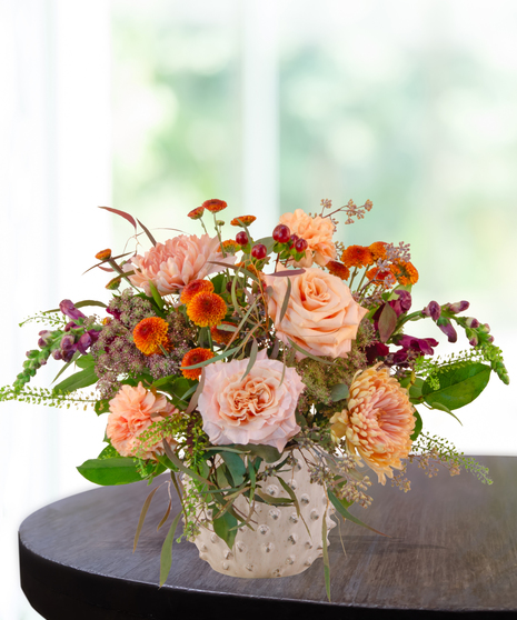 Peach, rust, and burgundy fall flower arrangement with roses, mums, snapdragons, and greenery in a white hobnail vase
