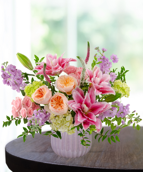 Spellbound flower arrangement with pink rose lilies, peach garden roses, pink spray roses, lavender stock, and green hydrangea in a soft blush vase