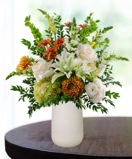 Topaz to Remember November birthday flower arrangement with white lilies, white roses, orange mums, and green Bells of Ireland in a white vase