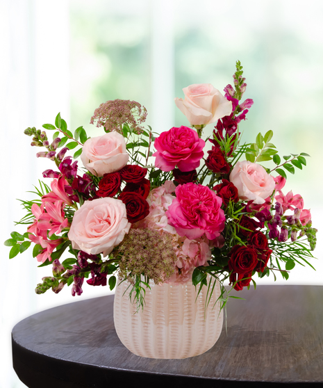 Vibrant floral arrangement featuring cranberry and blush roses in a textured cream vase for a January birthday gift.