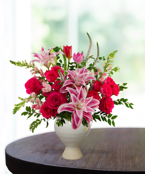 Legally Pink flower arrangement featuring hot pink roses, pink lilies, pink tulips, and white veronica in a matte cream ceramic pedestal vase.