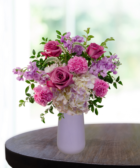 Pretty in Purple exclusive Valentine's and February birthday flower arrangement with lavender roses, white lilies, purple stock, and magenta mums in a frosted lavender vase.