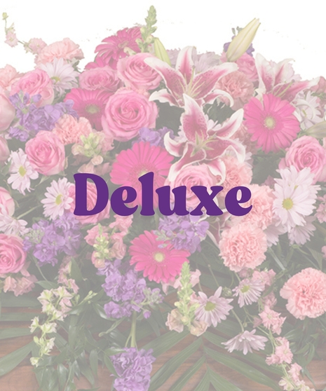 Feminine Casket Cover with pink roses, carnations, lilies, gerbera daisies, lavender stock, and purple daisies arranged over a wooden casket