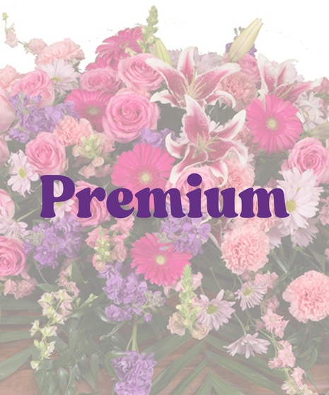 Feminine Casket Cover with pink roses, carnations, lilies, gerbera daisies, lavender stock, and purple daisies arranged over a wooden casket