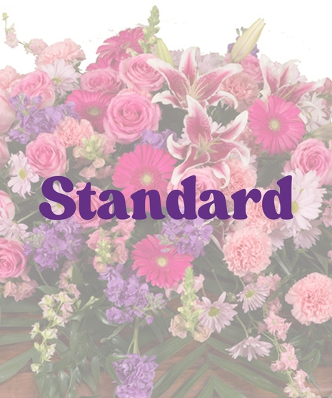 Feminine Casket Cover with pink roses, carnations, lilies, gerbera daisies, lavender stock, and purple daisies arranged over a wooden casket