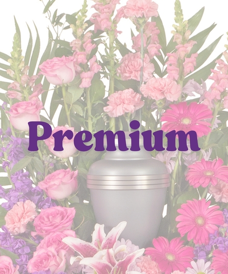 Feminine Cremation Arrangement featuring pink roses, carnations, gerbera daisies, rose lilies, purple stock, and tropical foliage surrounding a gray urn